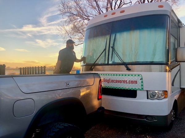 A man standing in the bed of a pickup truck, cleaning the windshield of an RV