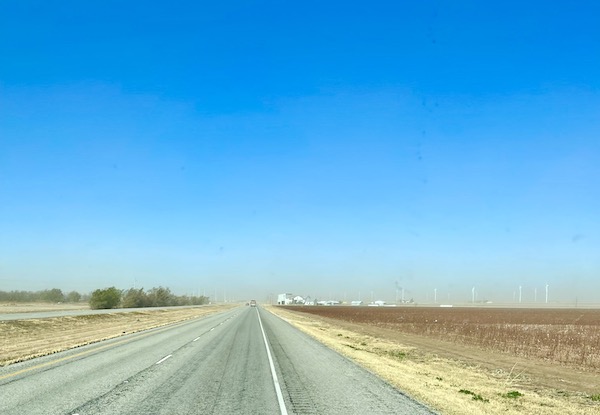 A highway with sand blowing in the distance.