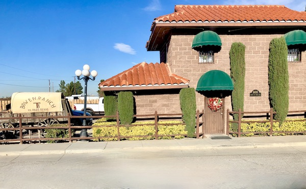 A brick building with barrel tile roof and green awnings.
