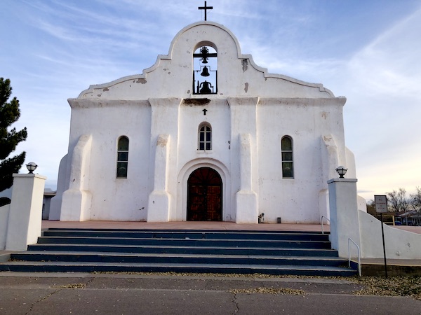 A large white, Spanish style church atop a flight of steps seen along the El Paso Texas Mission Trail