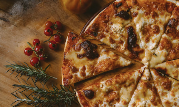 A sliced pizza on a pizza stone next to sprigs of rosemary and red berries from Enjoy Delicious Pizzas with a pizza stone