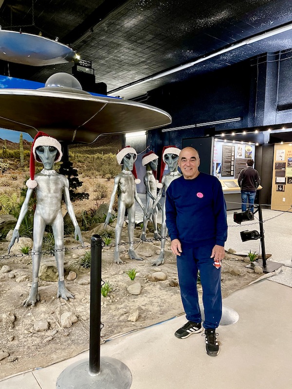 A man in navy sweats standing by a group of aliens with Santa hats at International UFO Museum Roswell NM