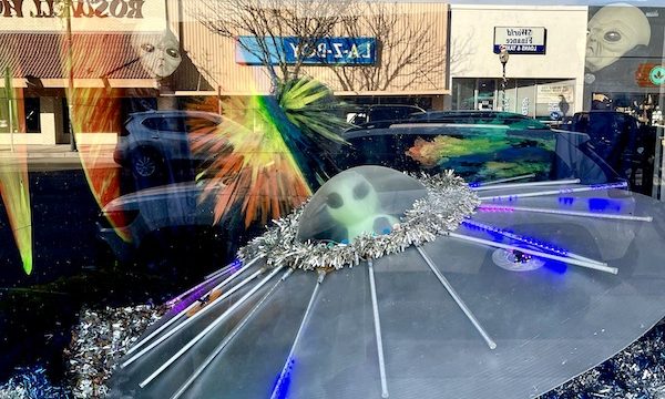 A flying saucer in a storefront window along with aliens at the International UFO Museum Roswell NM. The storefronts across the street are reflected in the glass.