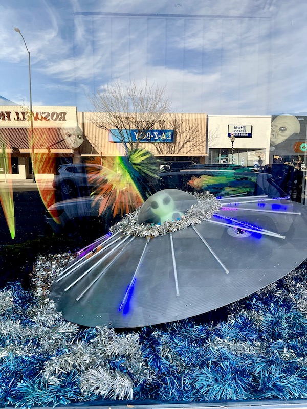 A flying saucer in a storefront window along with aliens at the International UFO Museum Roswell NM. The storefronts across the street are reflected in the glass.