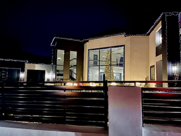 A mansion with an all gold Christmas tree visible in a ceiling to ground window.