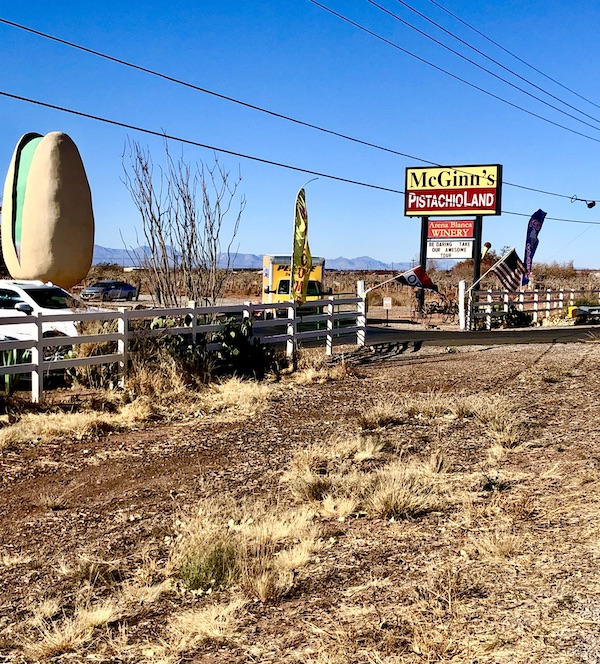 A field with a yellow sign and a huge white and green pistachio sculpture which is the World's Largest Pistachio Alamogordo NM