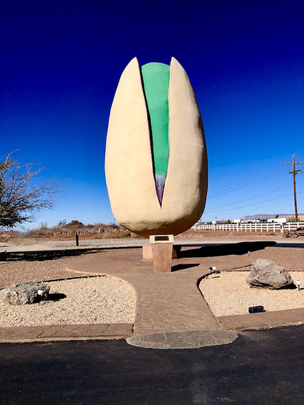 An enormous white and green pistachio sculpture in a park setting. The pistachio is the world's largest.