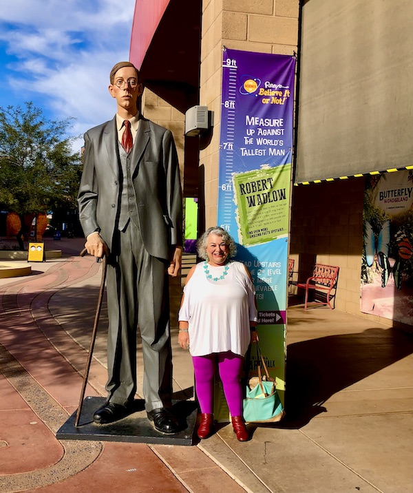 A short woman standing next to a life-sized statue of the world's tallest man outside Butterfly Wonderland Scottsdale AZ