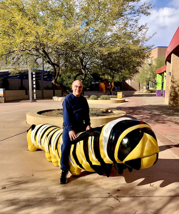 A man straddling a statue of a caterpillar at Butterfly Wonderland Scottsdale AZ