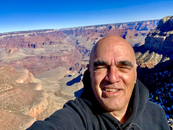 A man in a black sweatshirt with the Grand Canyon behind him, before our lunch at Fred Harvey Burger Grand Canyon AZ
