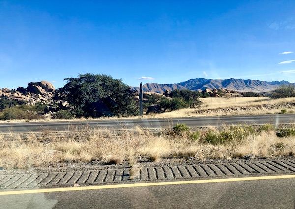 A highway view with black mountains and white rocks with a grove of trees in AZ.