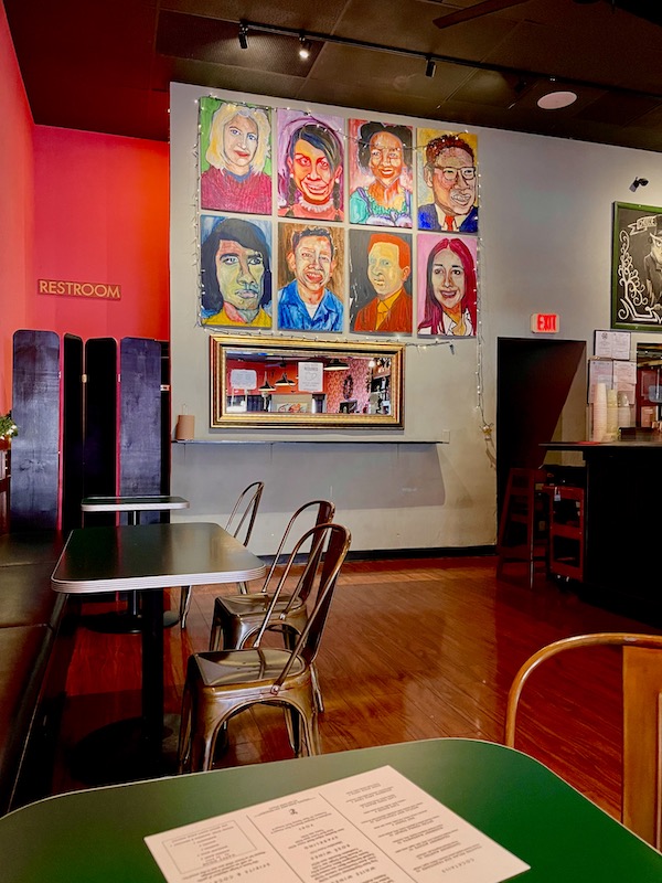 A wall in a restaurant with colorful portrait art on display.