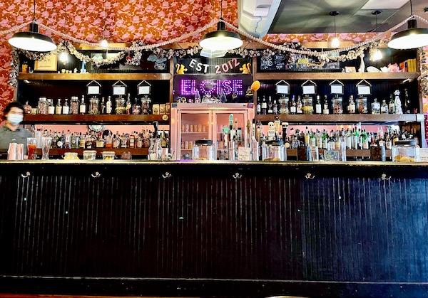 A black wood restaurant bar with shelves full of bottles and floral wall paper from Our Trip to Mexico and Lunch