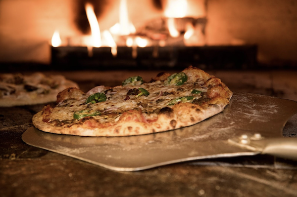 A freshly baked pizza on a metal pizza peal being taken from oven from The Essentials Behind Italian Cooking