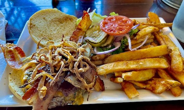 A white oblong plate topped with a burger, frizzled onions, lettuce tomato slice, pickle slices and fries at Haunted Hamburger Restaurant Jerome AZ
