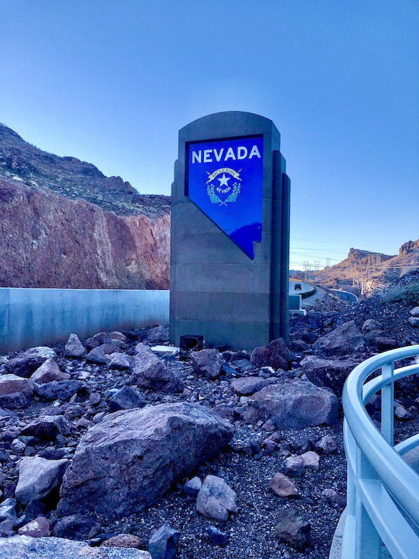 A monument standing in a rock bed with a bright blue square that says Nevada in white letters.