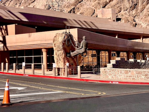 A bronze sculpture on the corner of a building of a man in hard hat scaling a mountain.