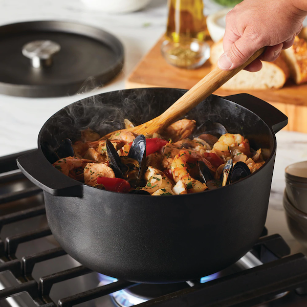 A black pot on a gas stove with a wooden spoon stirring the contents.