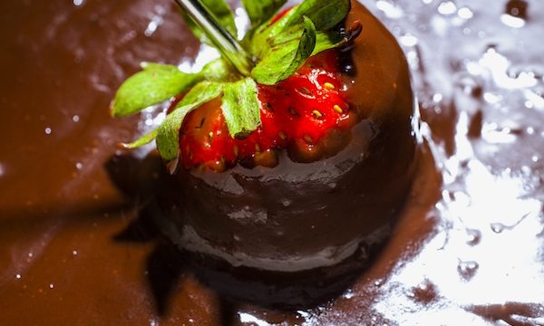 A red strawberry being dipped into melted chocolate fondue is one of my new warm weather favorites.
