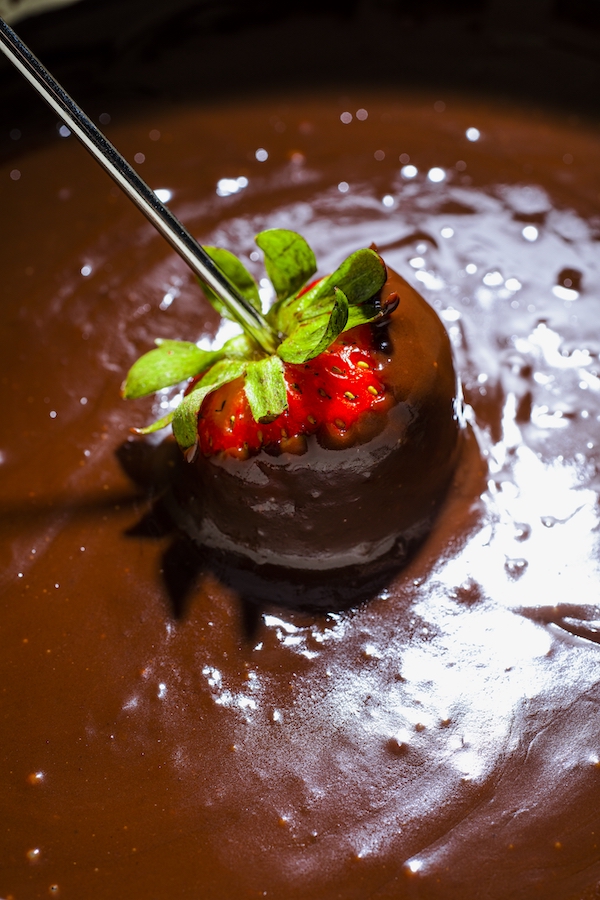 A red strawberry being dipped into melted chocolate fondue is one of my new warm weather favorites.