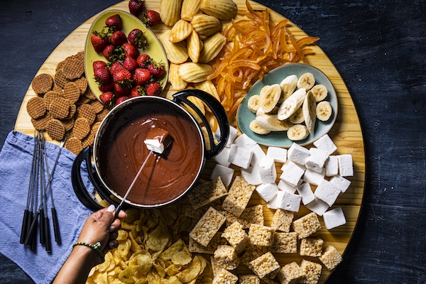 A large round board topped with chocolate fondue and assorted dipping items