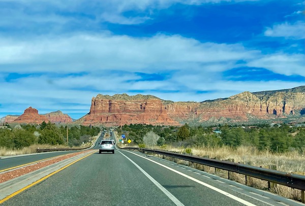 A highway with cars, trees, Red Rocks of Sedona Arizona and blue sky with puffy white clouds