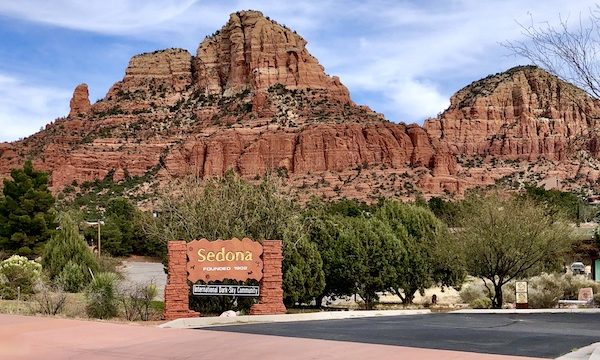 A red rock mountain formation and a brown sign tell you that you are visiting the Red Rocks of Sedona Arizona