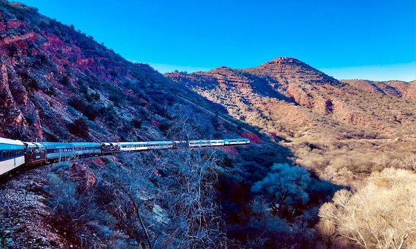 A train passing red rock mountains along the Verde Canyon Railroad Wilderness Route
