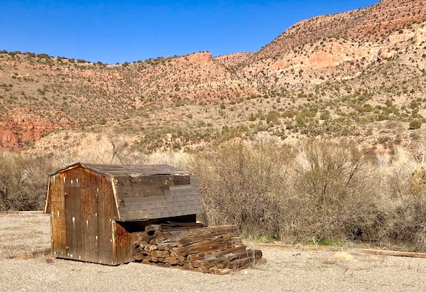 A wood shack with a pile of RR ties on the ground and mountains in the background along our Verde Canyon Railroad Wilderness Route