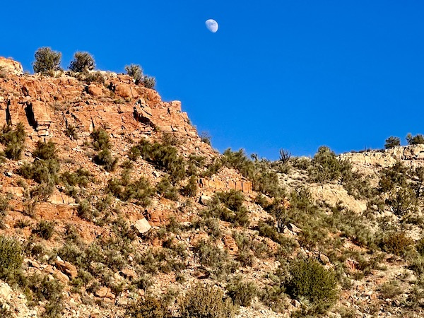 Mountainous terrain, clear deep blue sky and the moon.