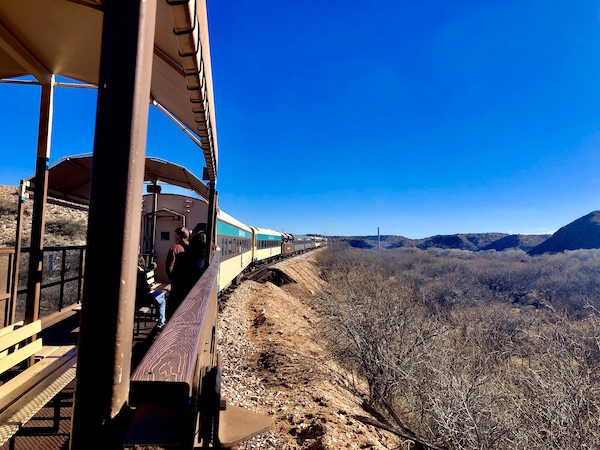 A train with an open air car passing black mountains along the Verde Canyon Railroad Wilderness Route