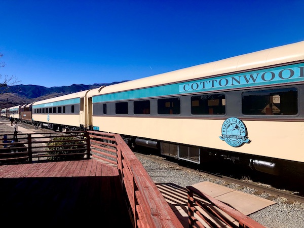 A cream colored train with burgundy and turquoise stripes is the Verde Canyon Railroad Wilderness Route train.