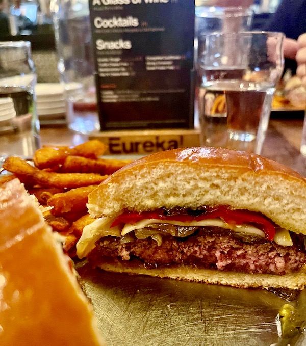 A half a burger in a bun with red pepper, jam and cheese.