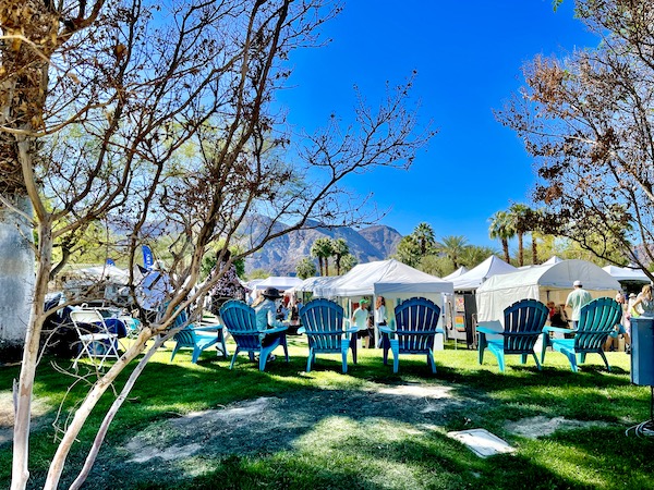 White tents set up in a park with lawn and a row of turquoise Adirondack chairs at La Quinta Art Celebration California