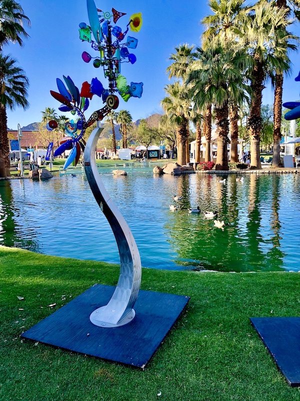 A mixed media sculpture of a tree by a lake with palm trees at La Quinta Art Celebration California