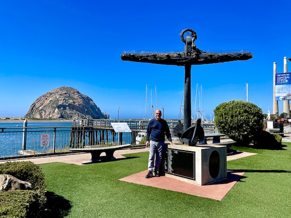 A man standing next to an anchor sculpture at Morro Bay California