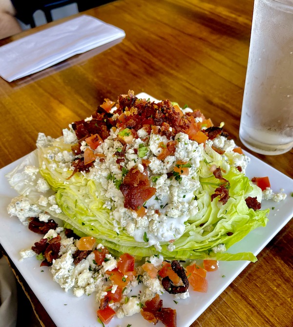 A large white square plate topped with half a head of iceberg lettuce, blue cheese, bacon and tomato in Morro Bay California