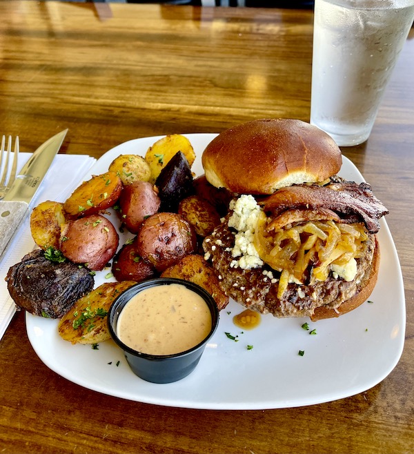 A white rounded square plate topped with a bacon cheeseburger with roasted potatoes and dip in Morro Bay California
