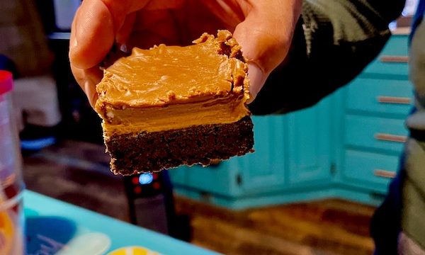 A man's hand holding a 3-layer peanut butter brownie.