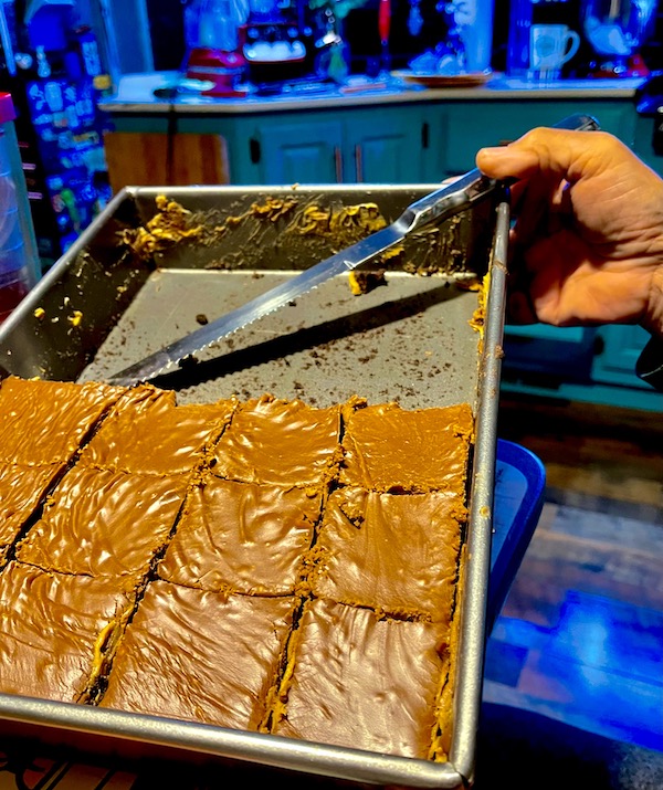 A baking pan partially filled with cut brownies. A man's handing is holding the tray for Peanut Butter Brownies Recipe