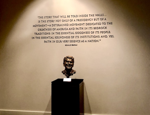 A black pedestal displaying a bronze bust of Ronald Reagan. The wall behind the bust has a quote of his at the Ronald Reagan Presidential Library