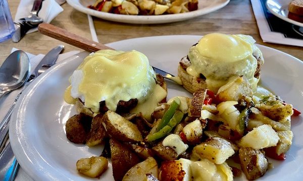 A large white plate topped with two poached eggs, crab cakes and potatoes at The Egg House Simi Valley CA