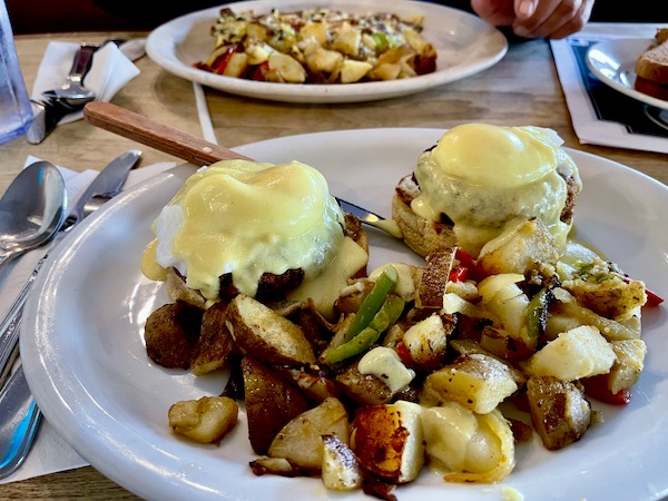 A large white plate topped with two poached eggs, crab cakes and potatoes at The Egg House Simi Valley CA