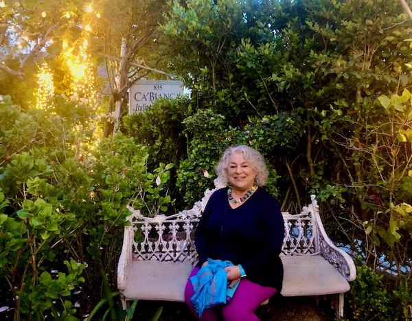 A woman with silver hair and a black tunic sitting on a white bench in a garden setting at Ca' Bianca Ristorante Italiano