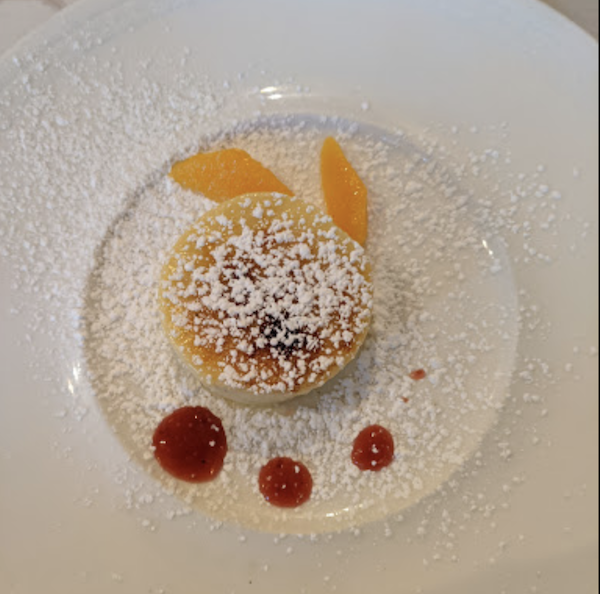 A white plate topped with a custard cake, dots of berry sauce and peach slices, dusted with powdered sugar at Ca' Bianca Ristorante Italiano