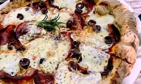 A whole pizza topped with cheese, salami and black olives at Café Reyes Pizza
