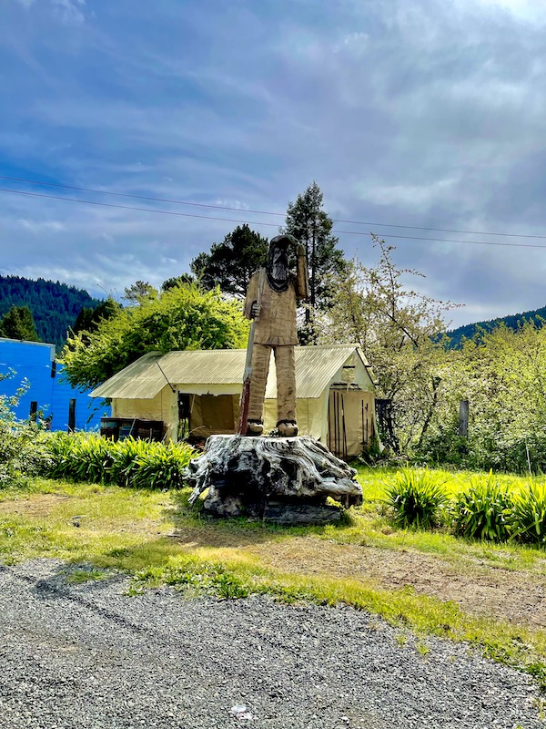 A cabin in the woods with a chainsaw sculpture of a man in front seen while driving the California Northern Coast Part I