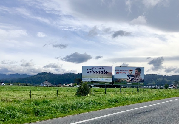 A grassy field with two road signs and mountains in the distance on the California Northern Coast Part II