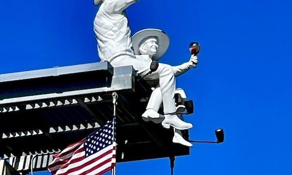 A pair of white sculptures of a woman and a man toasting with glasses of wine. They're sitting on the roof of a building that we toured while having Fun in Downtown Napa CA