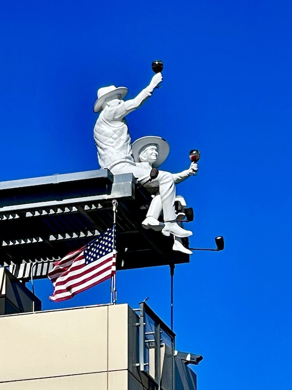 A pair of white sculptures of a woman and a man toasting with glasses of wine. They're sitting on the roof of a building that we toured while having Fun in Downtown Napa CA